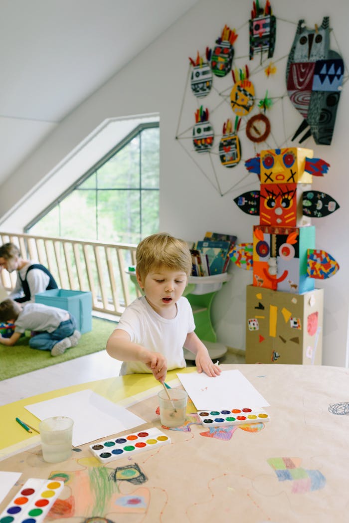 Young boy painting at a table in a colorful classroom setting.